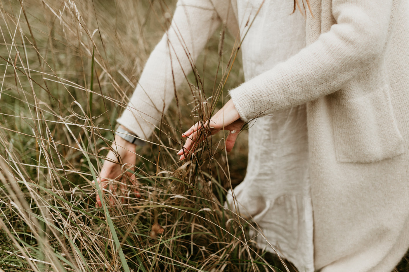 Hands touching tall dried grasses in a meadow